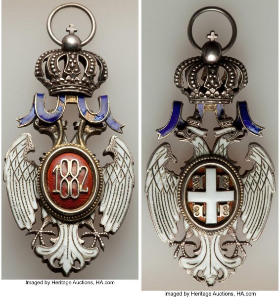Lot 32761 > Milan I Order of the White Eagle Third Class Commander Neck Badge ND (1883-1903) AU, Werlich-pp. 378-379, Barac-176. 65x34mm. 24.97gm. With crown-shaped suspension and ring. With white, red, and blue enamel. Type I, Model I. A striking presentation of this second highest decoration of Serbia, awarded for outstanding civil or military merit. Aside from some chipping in the enamel on the ribbon, the award appears very well preserved. 
