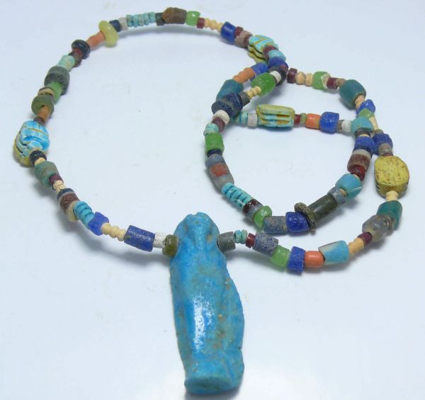 Egypte - Basse époque - Collier de perles diverses (oushebti) - 664-332 av. J.-C. - (26ème-30ème dynastie) Très beau collier de perles de silice et de perles en pâte de verre aux couleurs variées, intercalées de 4 scarabées en fritte émaillée bleue et se terminant par un oushebti en fritte émaillée bleue. 292 mm