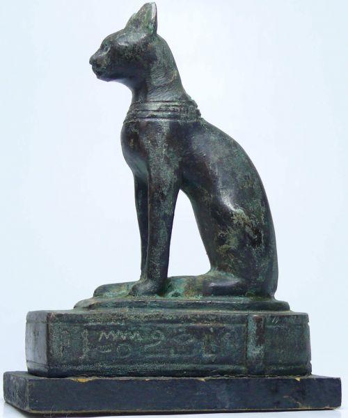 Egypte - Grande statuette de Bastet en bronze - Ancien travail égyptien, ou de style saïte Grande statuette en bronze représentant la déesse Bastet sous sa forme animale, le chat. Elle est assise dans une attitude digne, les pattes avant bien droites et la queue le long du corps, sur un socle inscrit de nombreux hyéroglyphes. Quelques traces de patine vert olive. 155x120x59 mm.