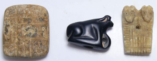 Moyen-Orient - Lot de 2 amulettes et d'une plaquette en terre cuite - 2000 / 1500 av. J-C. Lot composé d'une amulette en obsidienne représentant un animal, d'une plaquette en pierre beige représentant une idole jumelle zoomorphe et d'une plaquette en terre cuite à cartouches multiples. De 25 à 30 mm.